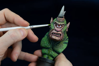Person painting a small green creature bust with a Ghost brush on a black background